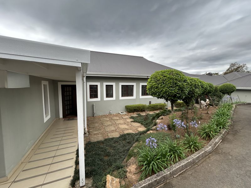 Front exterior view of the townhouse featuring a covered entrance, tiled walkway, and well-maintained landscaped garden with paved pathways.