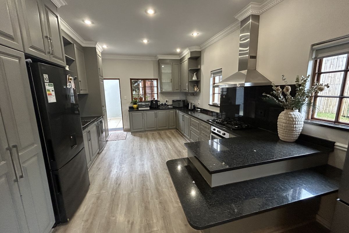Modern kitchen featuring grey shaker-style cabinetry, dark granite countertops, stainless steel gas hob, extractor fan, and recessed lighting with wood-look laminate flooring.
