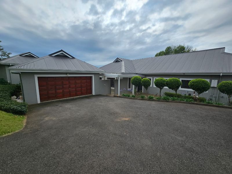 Front exterior view of the townhouse featuring a paved driveway, double garage, and well-maintained garden beds with manicured shrubs.