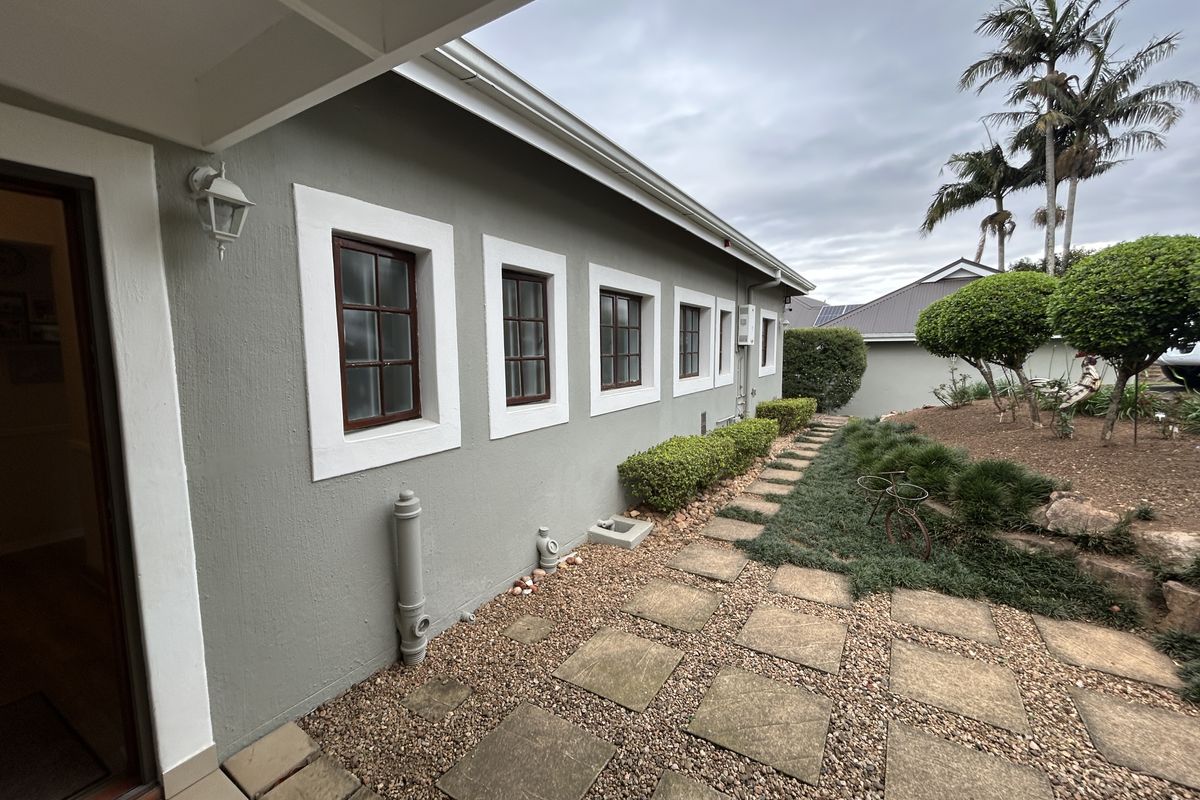 A well-maintained rear exterior view of the townhouse featuring a paved walkway, gravel landscaping, and established garden beds along the side wall.