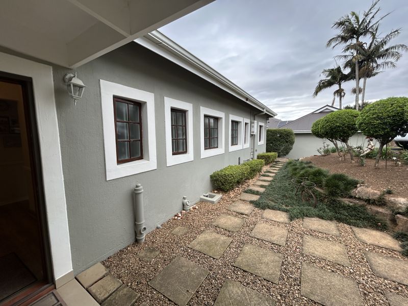 A well-maintained rear exterior view of the townhouse featuring a paved walkway, gravel landscaping, and established garden beds along the side wall.