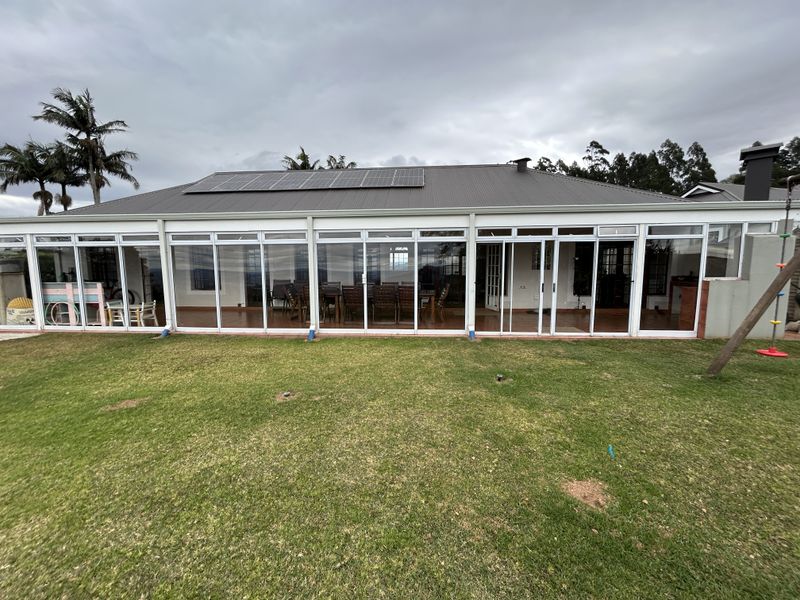 Rear view of the townhouse featuring an enclosed patio with extensive sliding glass doors, a metal roof, and installed solar panels overlooking the garden.