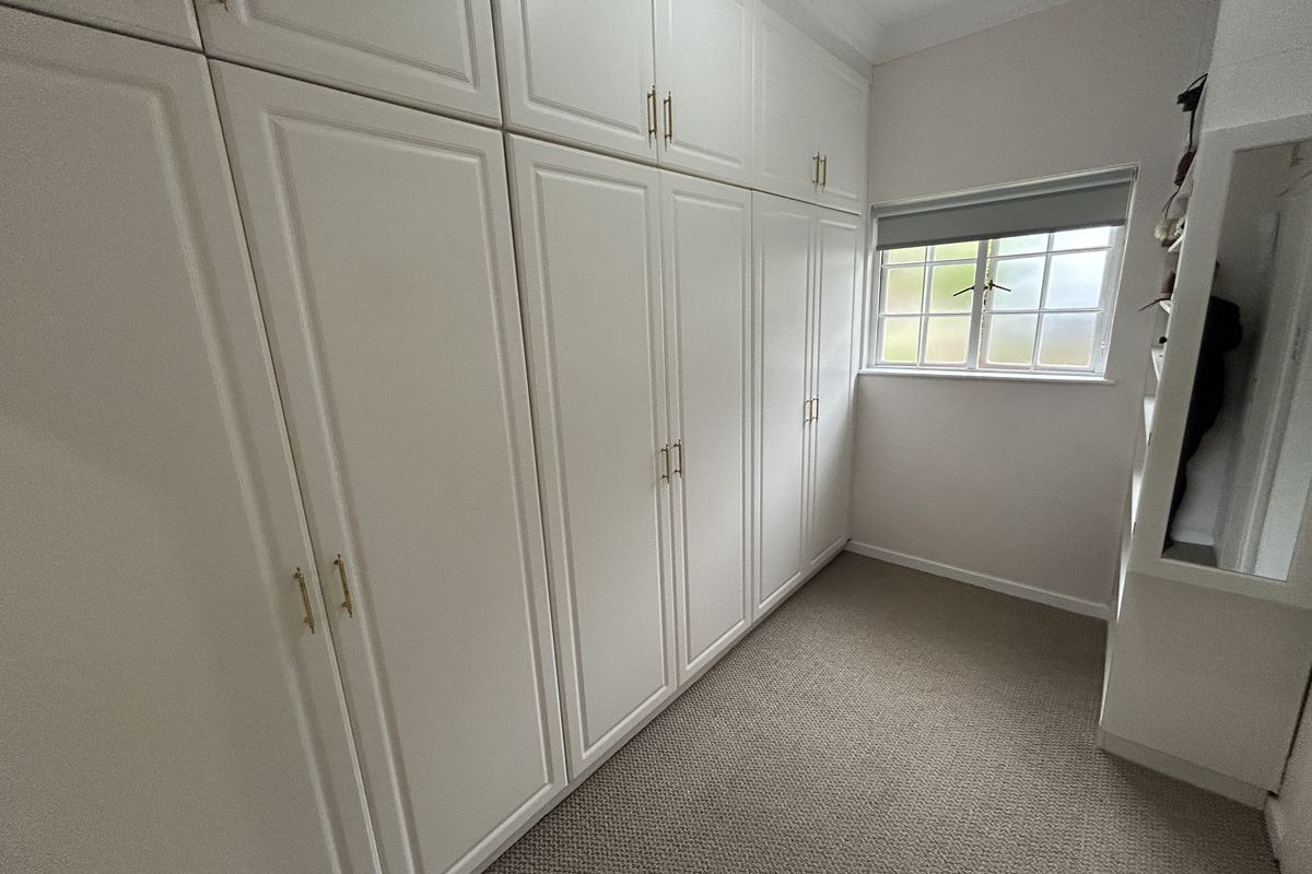 A clean, well-maintained bedroom featuring extensive floor-to-ceiling built-in cabinetry, neutral carpeting, and a window with a roller blind.