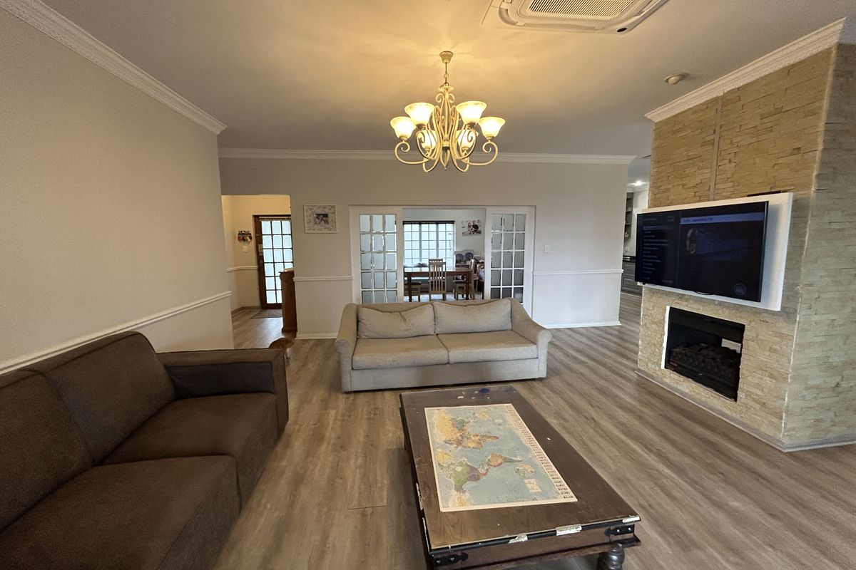 Spacious living room featuring a stone-clad fireplace, crown molding, wainscoting, and modern laminate flooring, with integrated ceiling air conditioning and french doors.
