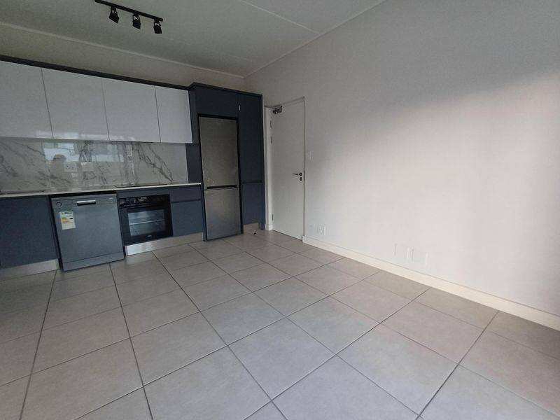 Modern open-plan kitchen featuring sleek cabinetry, marble-look splashback, integrated appliances, and neutral tiled flooring in a clean, vacant space.
