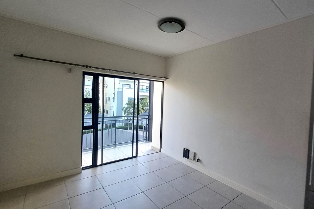 An empty, well-lit living area featuring neutral tiled flooring and a sliding glass door that opens onto a private balcony.
