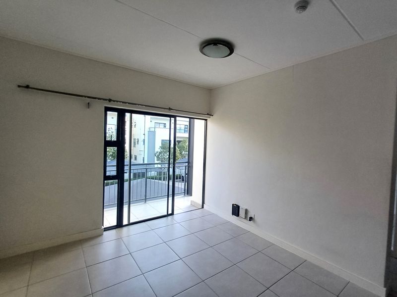 An empty, well-lit living area featuring neutral tiled flooring and a sliding glass door that opens onto a private balcony.
