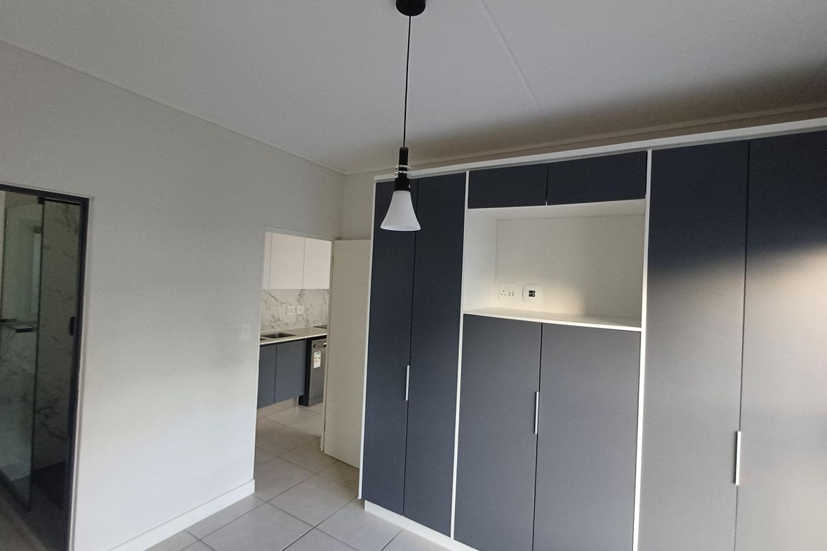 A modern bedroom featuring neutral tiled flooring, ample built-in cupboard storage, and a contemporary pendant light fixture.