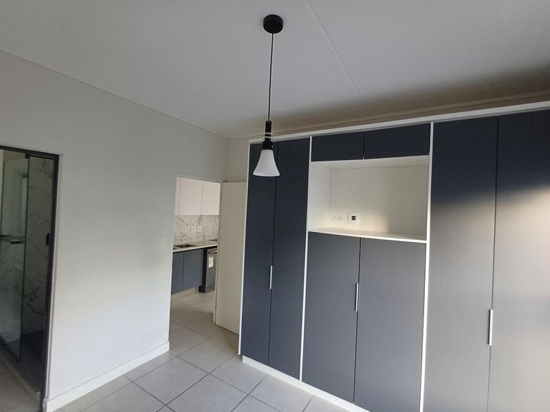 A modern bedroom featuring neutral tiled flooring, ample built-in cupboard storage, and a contemporary pendant light fixture.
