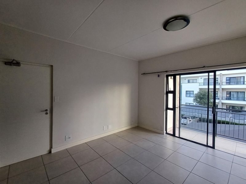 A bright, empty living area featuring neutral tiled flooring and a large sliding glass door providing direct access to a private balcony.