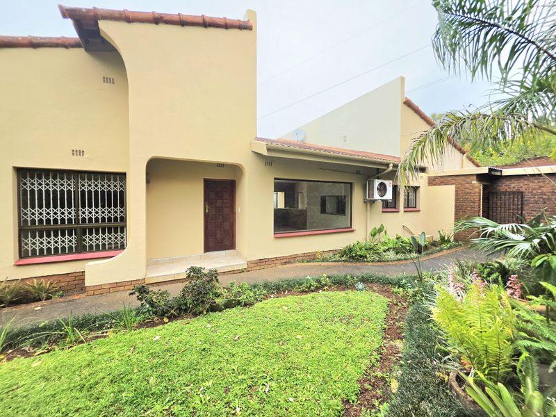Rear exterior view of the house featuring a paved walkway, landscaped garden, security bars on windows, and an external air conditioning unit.