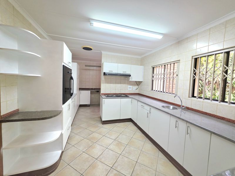 A functional kitchen featuring white built-in cabinetry, laminate countertops, a gas hob, built-in oven, and tiled finishes throughout.