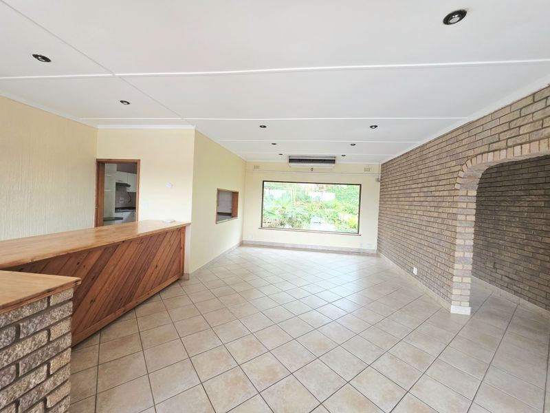 Spacious living area featuring a built-in bar, exposed brick wall with an archway, tiled flooring, and large windows providing natural light.