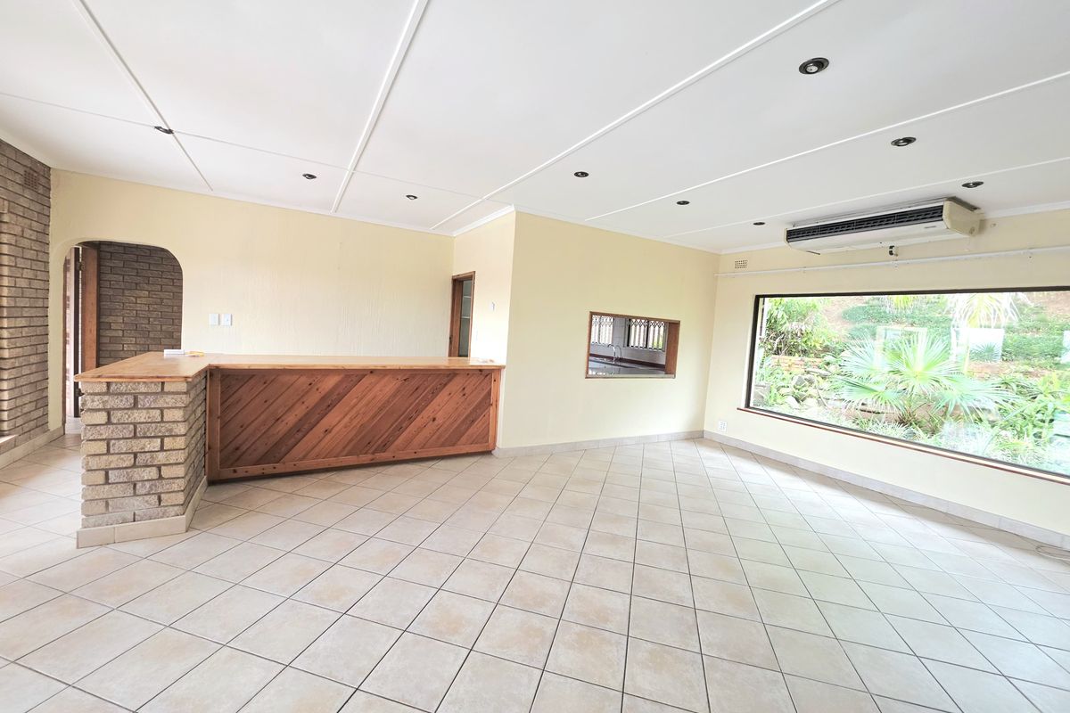 Spacious living area featuring a built-in brick bar, tiled flooring, and a large window overlooking the garden, offering a versatile open-plan layout.