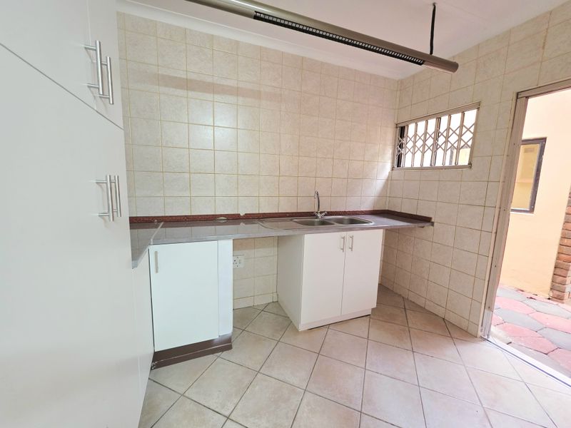 A functional scullery area featuring built-in white cabinetry, a double bowl sink, tiled splashbacks, and direct access to the exterior.