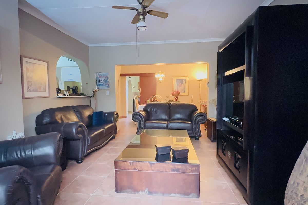 A spacious living room featuring tiled flooring, a ceiling fan, and an open-plan layout with an archway leading to the dining area.