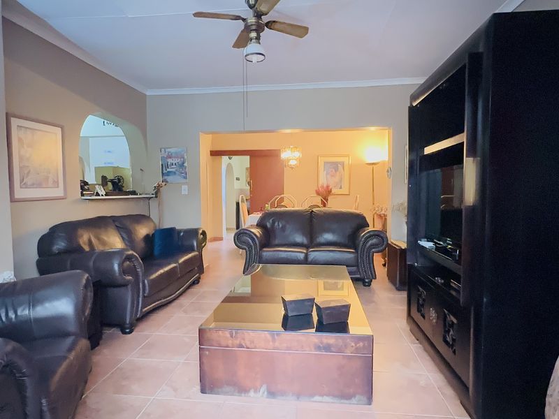 A spacious living room featuring tiled flooring, a ceiling fan, and an open-plan layout with an archway leading to the dining area.