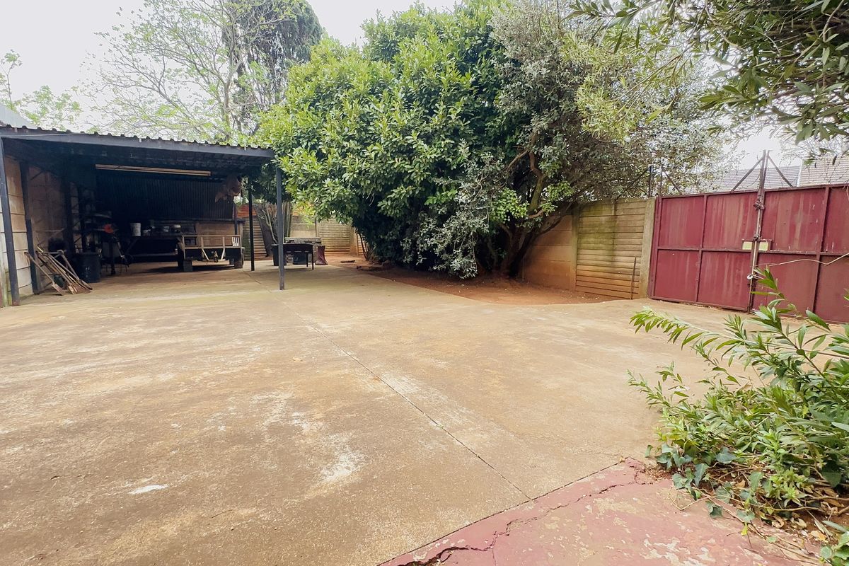 Spacious rear yard featuring extensive concrete paving, a covered patio area, and secure metal perimeter gates, offering potential for outdoor landscaping or entertainment space.