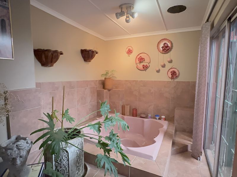 A bathroom featuring a built-in pink bathtub with tiled surround, tiled flooring, and sliding glass doors providing access to the exterior.