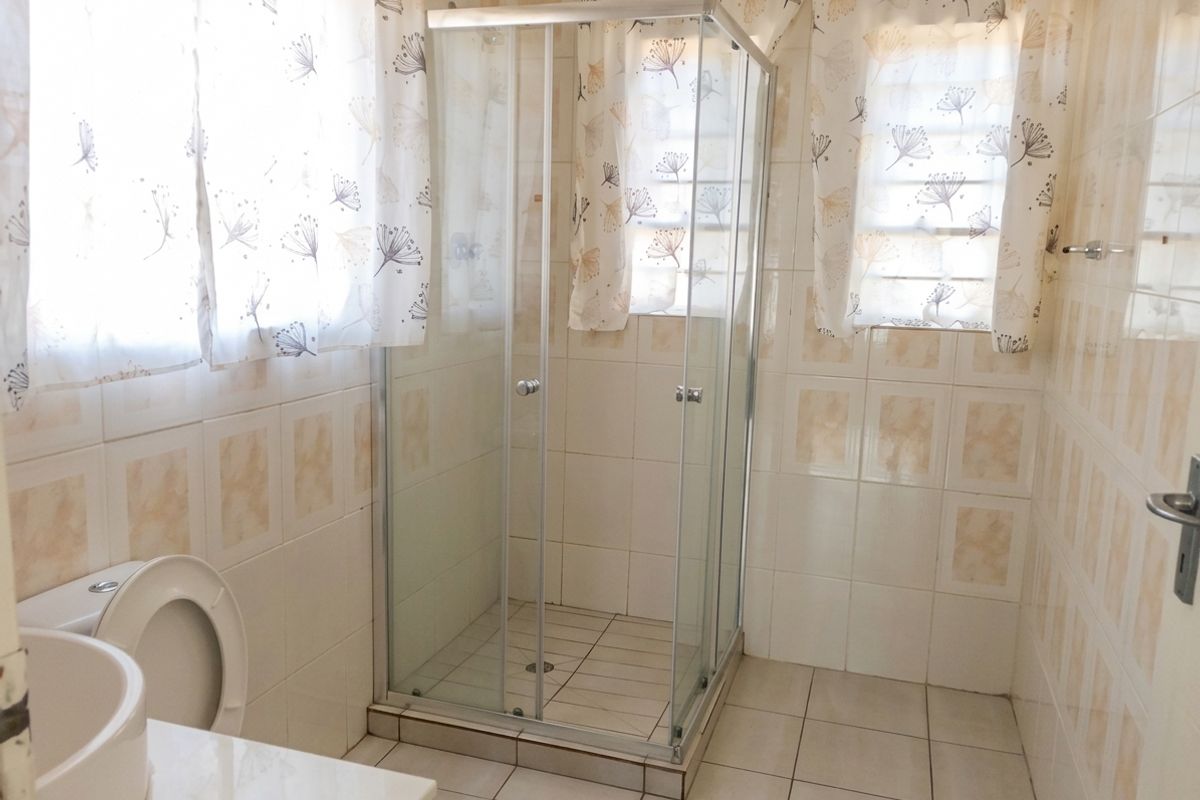 A functional bathroom featuring a glass shower enclosure, a toilet, and a vanity basin with neutral wall and floor tiling.