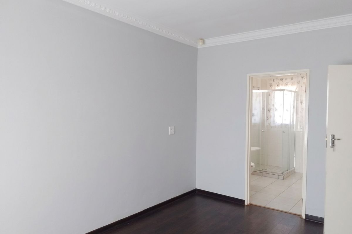 A clean, empty bedroom featuring dark laminate flooring, white walls, and decorative ceiling cornicing, with an adjoining en-suite bathroom visible through the doorway.