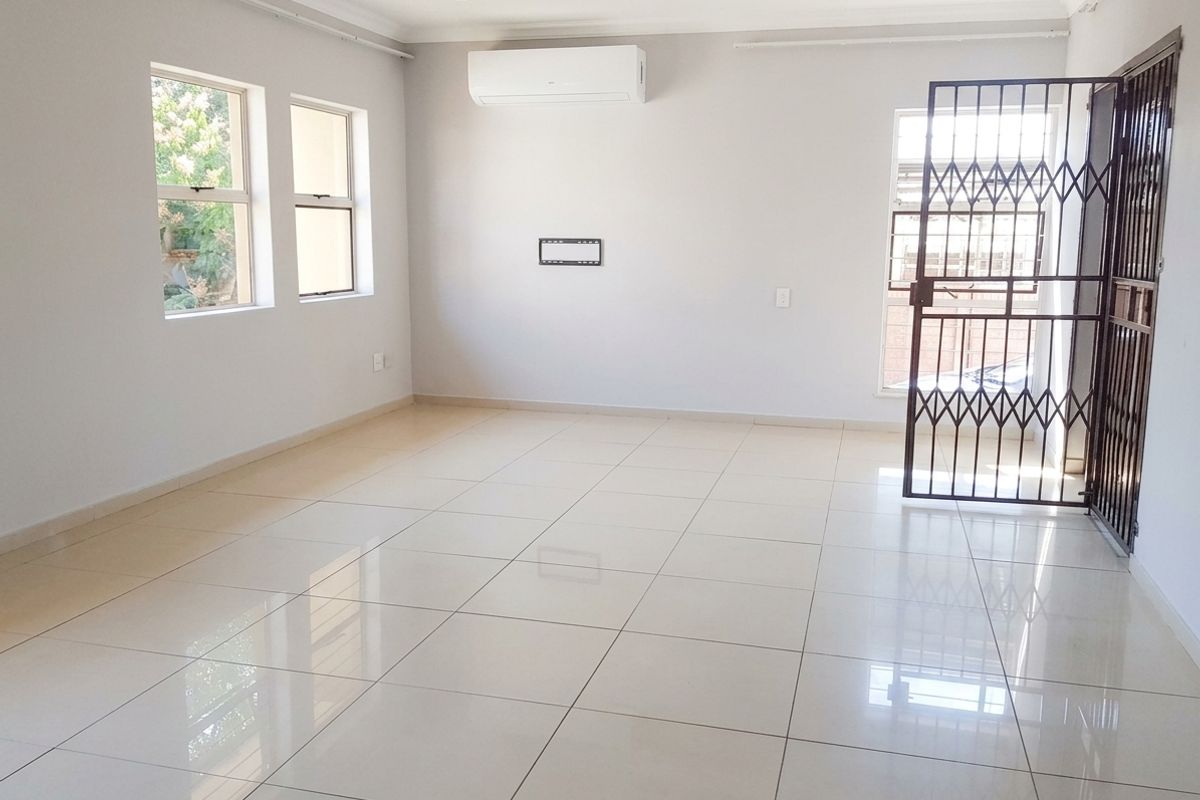 A bright, empty living room featuring neutral tiled flooring, a wall-mounted air conditioning unit, and a secure metal entrance gate.