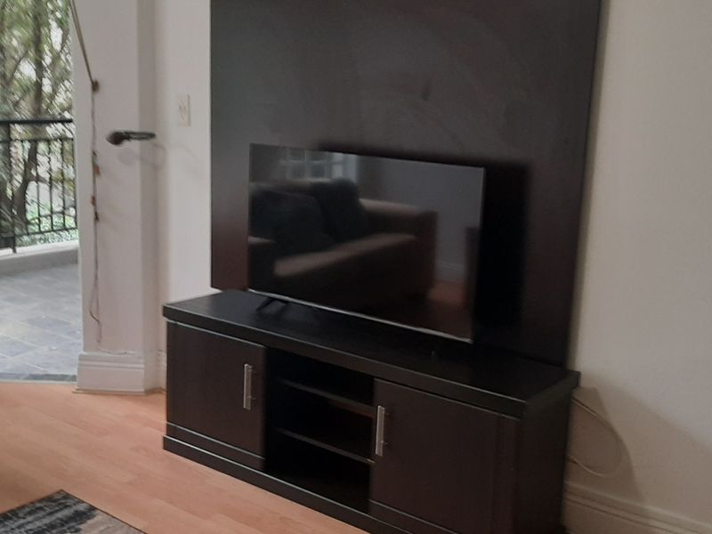 A living room area featuring laminate flooring and a built-in dark wood media wall panel, with direct access to an outdoor balcony.