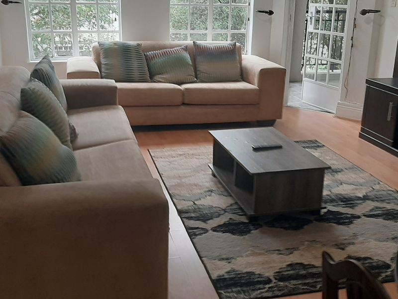A comfortable living room featuring laminate flooring, large multi-pane windows, and classic french doors leading to an outdoor area.