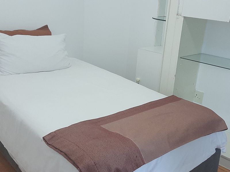 A compact bedroom featuring laminate flooring and built-in white cabinetry with integrated glass shelving.