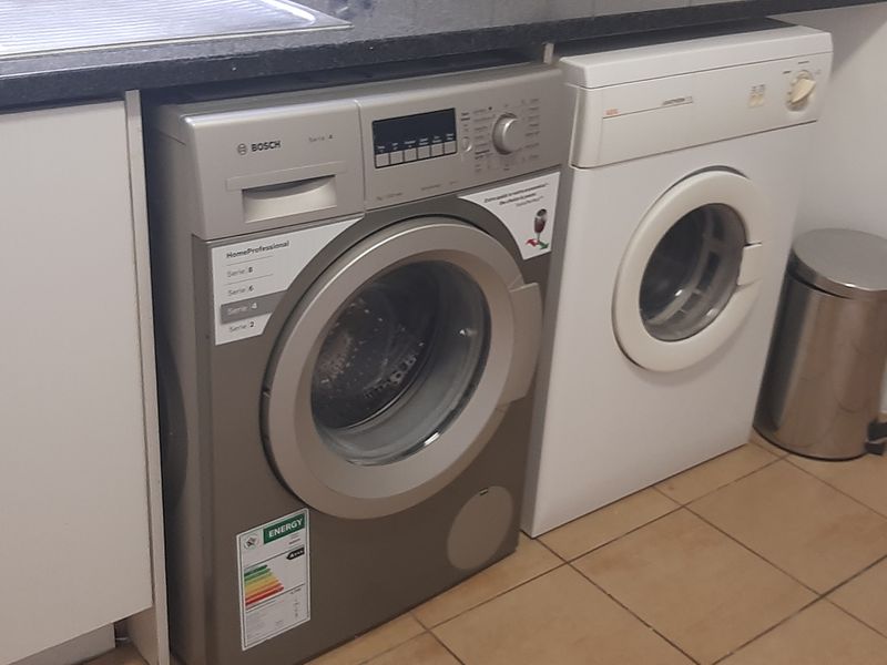 A functional laundry area featuring tiled flooring, a stainless steel sink, and built-in cabinetry with space for under-counter appliances.