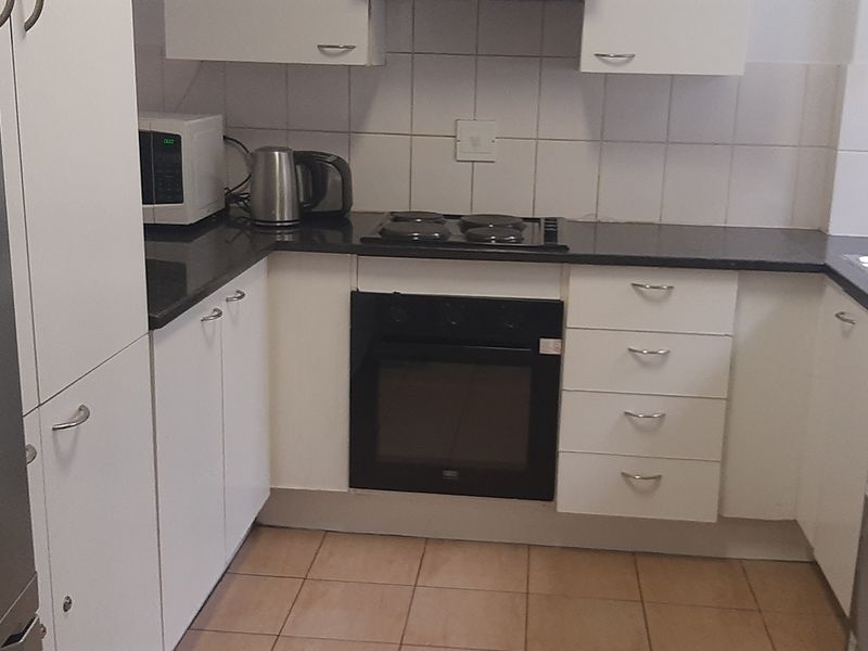 A functional kitchen featuring white cabinetry, dark granite countertops, an electric hob, built-in oven, and tiled finishes.