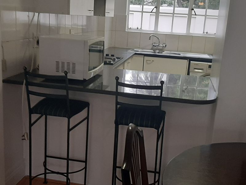 A functional kitchen featuring granite countertops, built-in cabinetry, a stainless steel sink, and a tiled backsplash, with a breakfast bar overlooking the dining area.