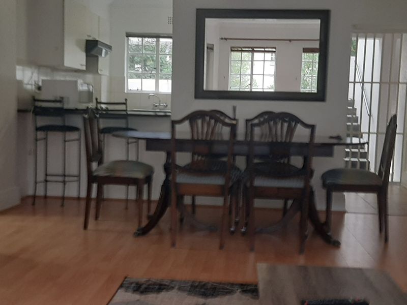 Open plan living and dining area featuring laminate flooring and an integrated kitchen space with cabinetry and an extractor fan.