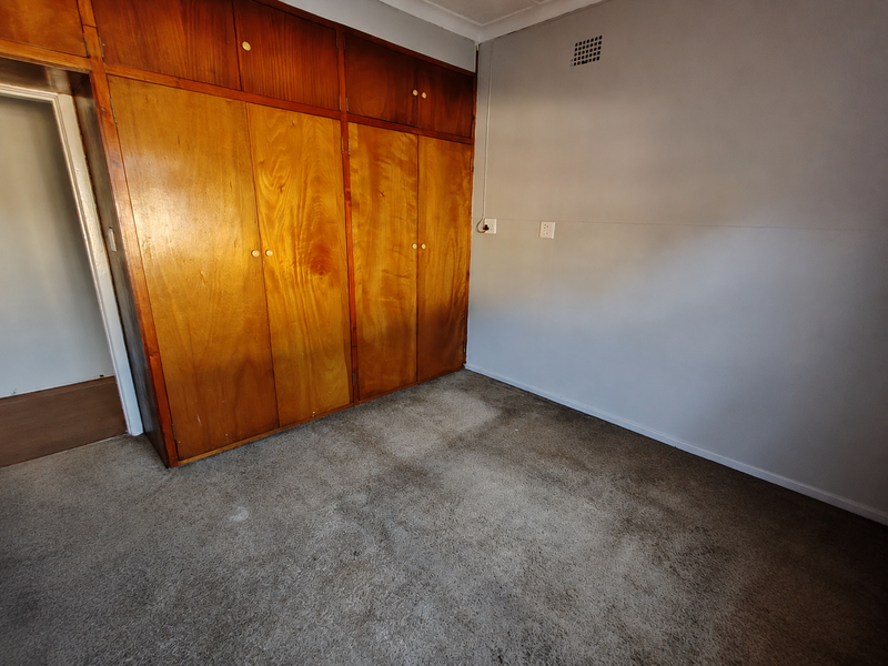 A vacant bedroom featuring built-in wooden cupboards and carpeted flooring, providing a blank canvas for potential updates and interior design.