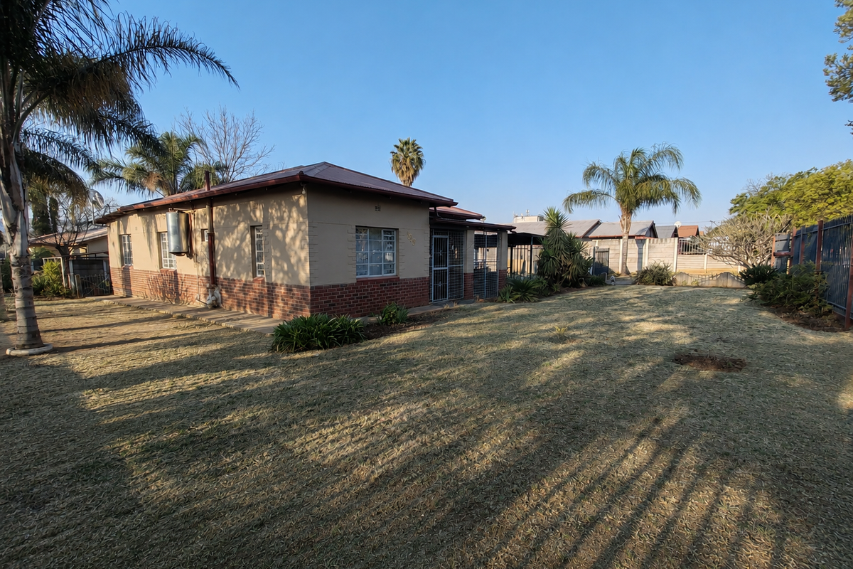Rear view of the house featuring a brick and plaster facade, metal roofing, and a spacious garden with perimeter walling.