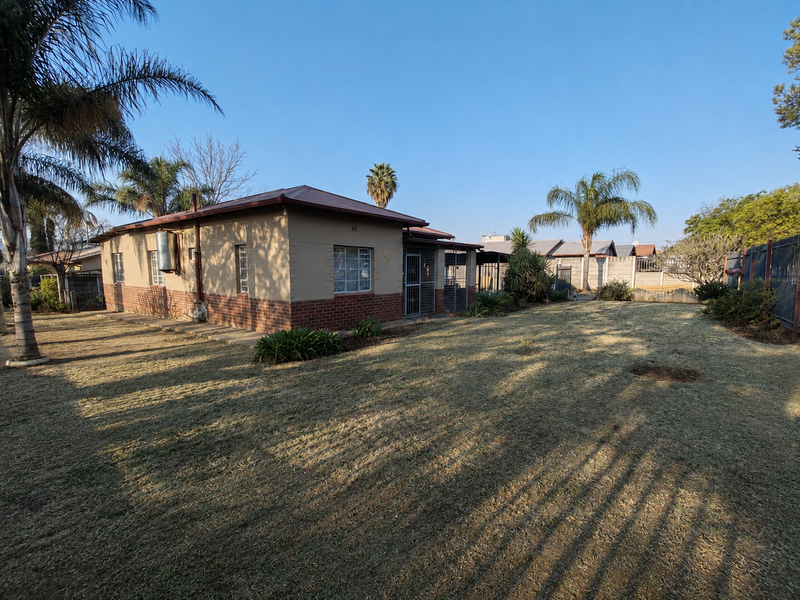 Rear view of the house featuring a brick and plaster facade, metal roofing, and a spacious garden with perimeter walling.