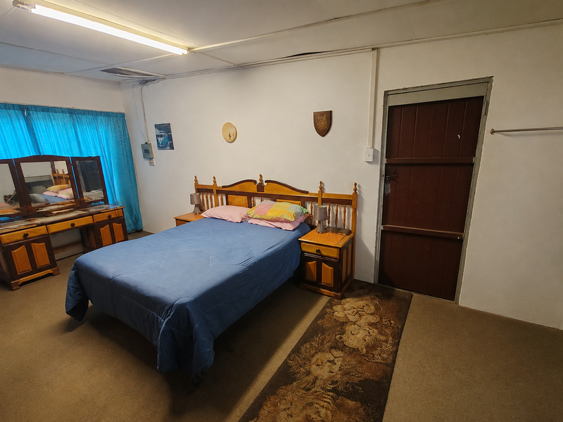 A dated bedroom featuring carpeted flooring, a timber door, and exposed electrical conduit, offering potential for modernization and cosmetic updates.