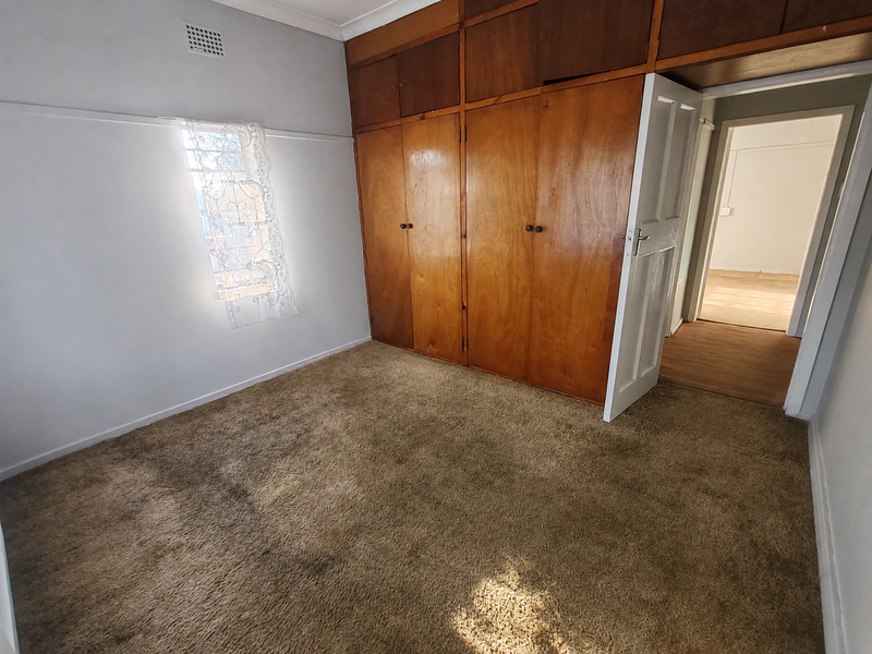A vacant bedroom featuring built-in wooden cupboards and carpeted flooring, offering a blank canvas for potential renovation and modernization.