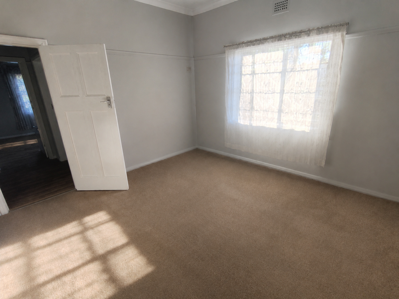 A bright, empty bedroom featuring neutral wall paint, carpeted flooring, and a classic picture rail, offering a clean canvas for personalization.