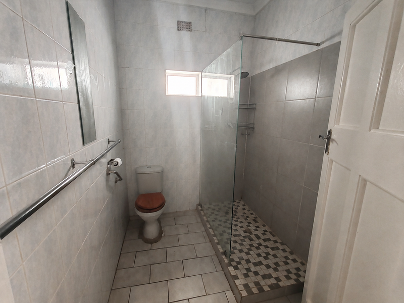A functional bathroom featuring a walk-in shower with a glass screen, tiled walls and flooring, and a standard toilet.