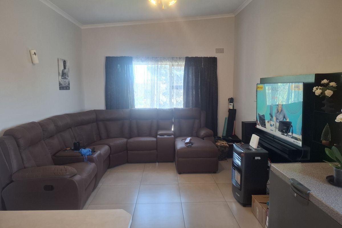 A spacious living room featuring neutral tiled flooring, a ceiling fan, and large windows, providing a comfortable and functional area for relaxation.