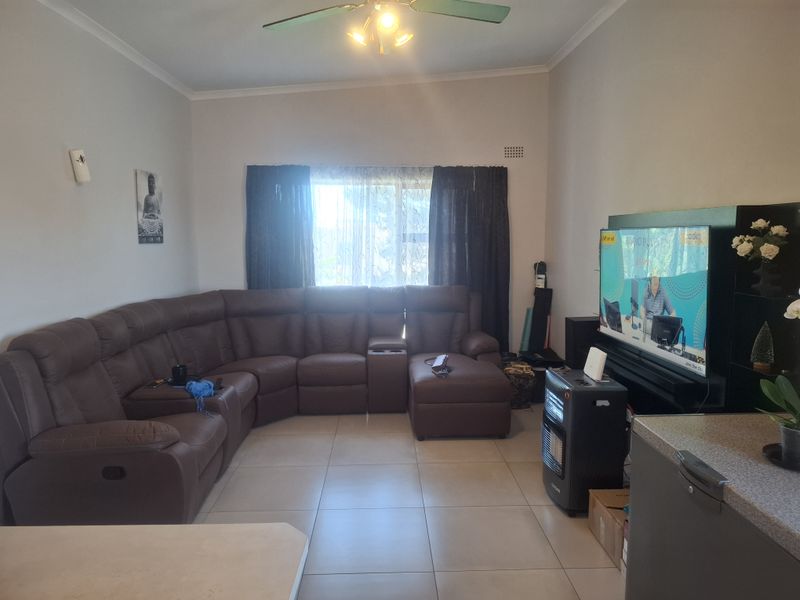 A spacious living room featuring neutral tiled flooring, a ceiling fan, and large windows, providing a comfortable and functional area for relaxation.