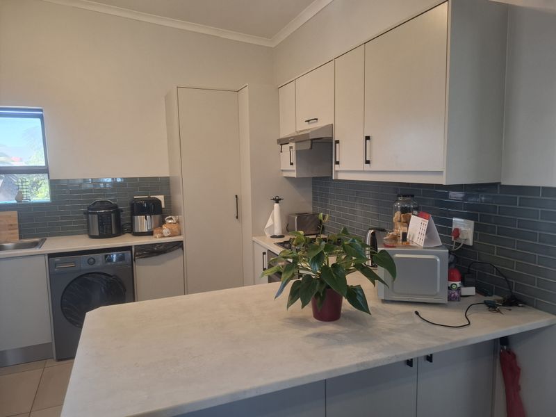 A functional kitchen featuring modern grey subway tile backsplash, ample built-in cabinetry, a central island, and integrated laundry facilities.