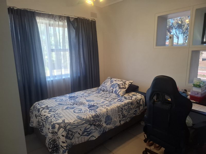 A functional bedroom featuring tiled flooring, a ceiling fan, and unique recessed wall shelving, providing a practical space for rest or study.