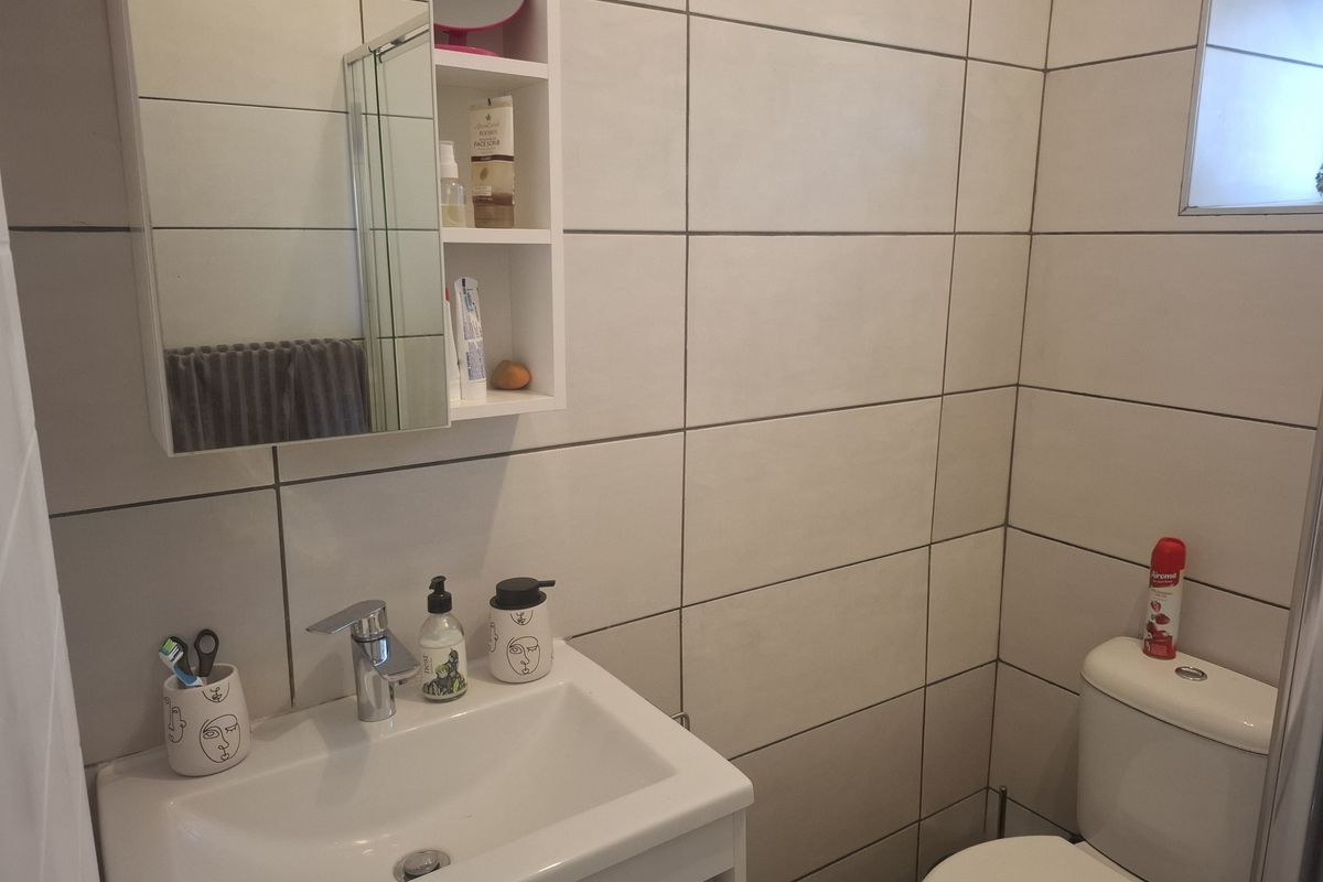 A compact, modern bathroom featuring a vanity cabinet with basin, wall-mounted medicine cabinet, and neutral ceramic wall tiling.
