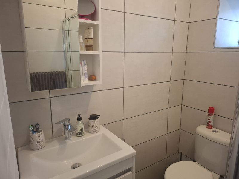 A compact, modern bathroom featuring a vanity cabinet with basin, wall-mounted medicine cabinet, and neutral ceramic wall tiling.