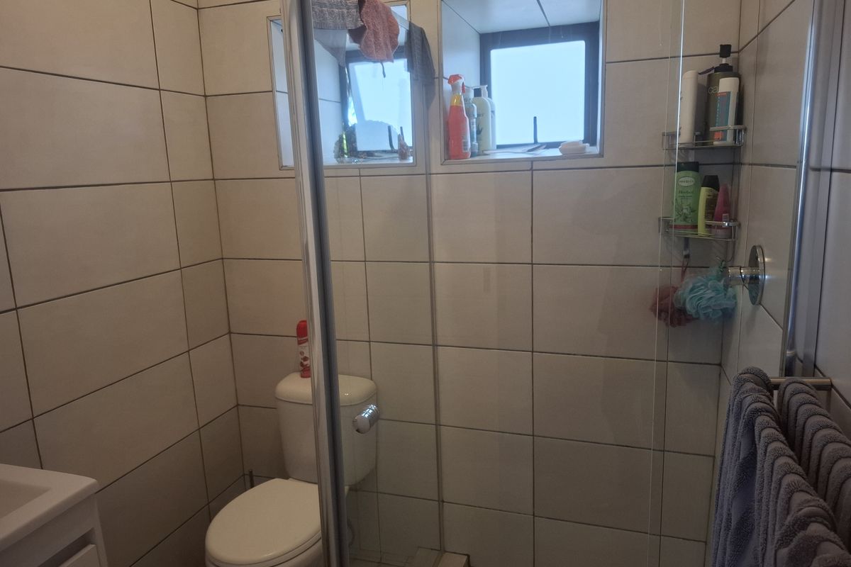A functional bathroom featuring a glass-enclosed shower, toilet, and neutral wall tiling with a recessed window for natural light.