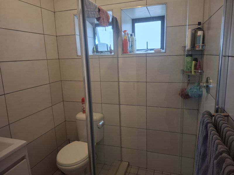 A functional bathroom featuring a glass-enclosed shower, toilet, and neutral wall tiling with a recessed window for natural light.