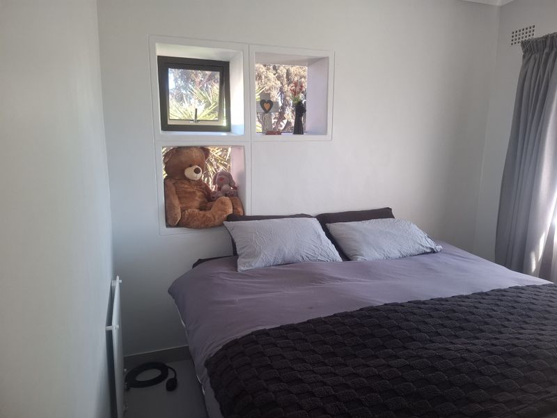 A bedroom featuring unique recessed wall shelving, a wall-mounted heater, and a window with curtain tracks.
