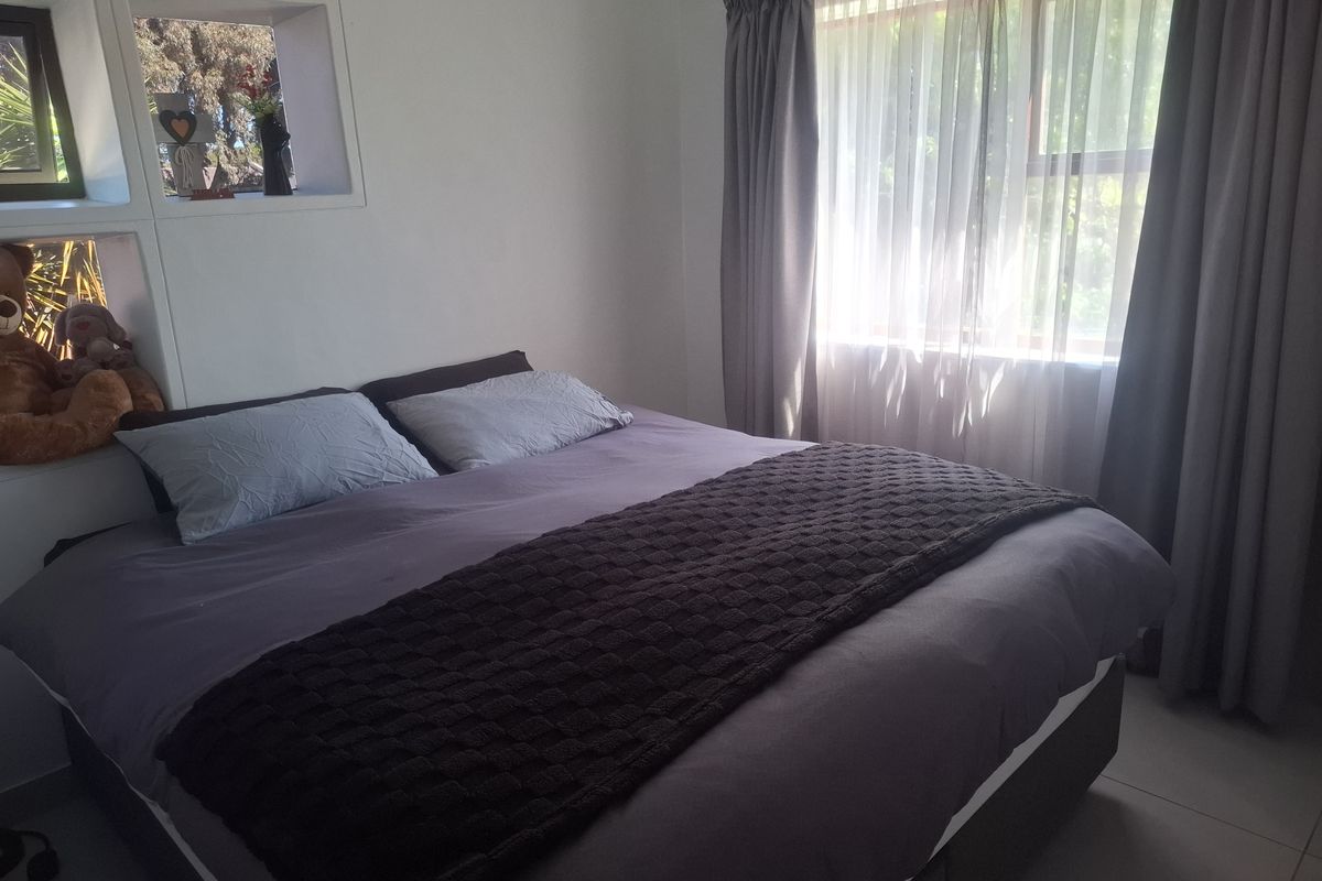 A comfortable bedroom featuring a built-in wall niche for storage and a large window with curtains allowing natural light.